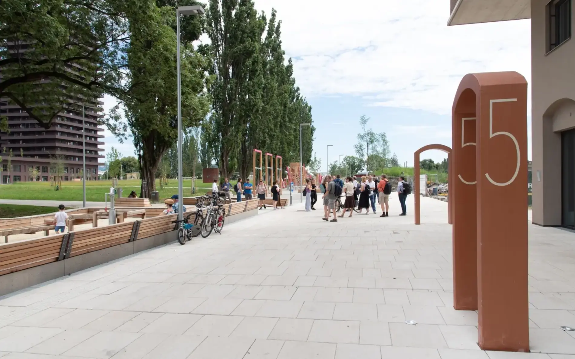 Siedlung mit breitem Geh- und Radweg. Am Rand einige Sitzbänke und Begrünung.
