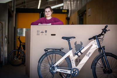 Fahrrad mit einem Holzrahmen, dahinter steht eine Frau