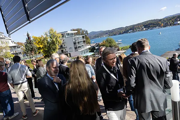 Menschen auf einer Terrasse reden miteinander, im Hintergrund der Wörthersee