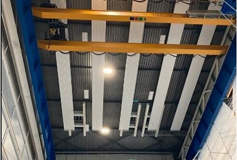 Deckenansicht einer Industriehalle mit neu installierten LED-Leuchten und gelben Kranträgern.