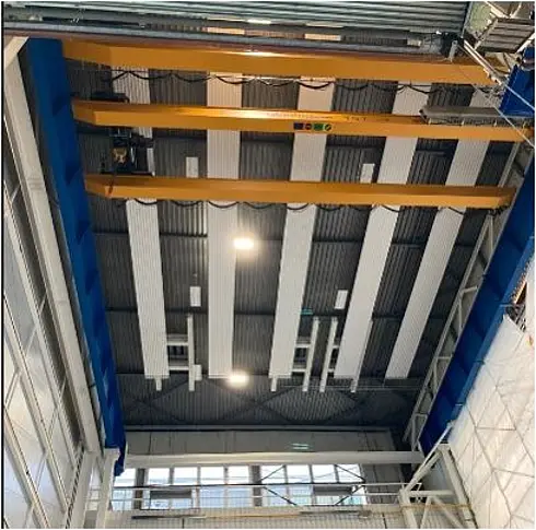 Deckenansicht einer Industriehalle mit neu installierten LED-Leuchten und gelben Kranträgern.