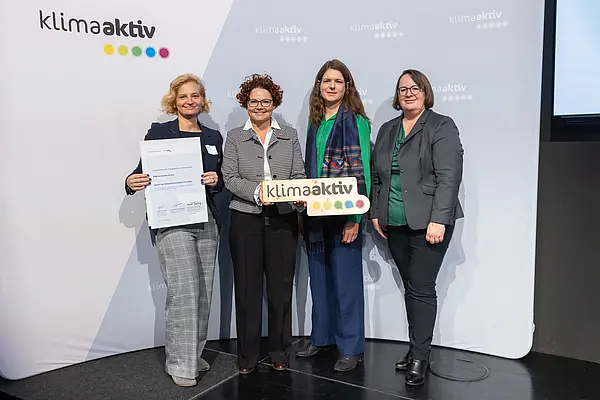 4 Personen mit Urkunde und klimaaktiv Schild schauen in die Kamera