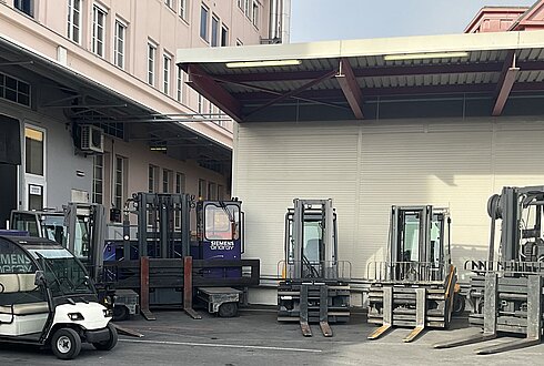 Mehrere Elektro-Stapler und ein kleines Elektrofahrzeug vor einer Werkshalle.