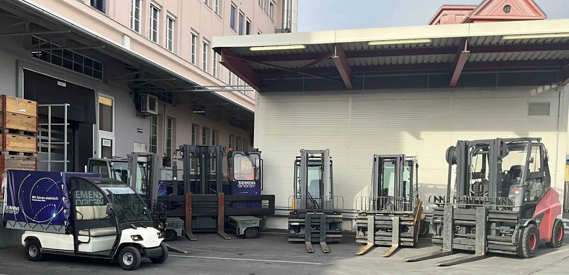 Mehrere Elektro-Stapler und ein kleines Elektrofahrzeug vor einer Werkshalle.