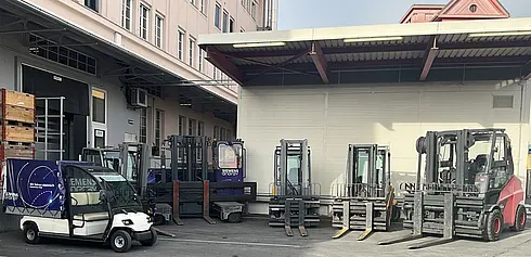 Mehrere Elektro-Stapler und ein kleines Elektrofahrzeug vor einer Werkshalle.