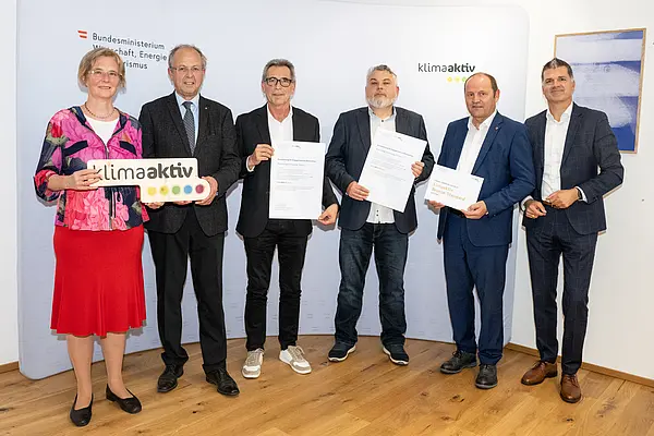 eine Gruppe von Menschen auf einer Bühne hält Urkunden in die Kamera