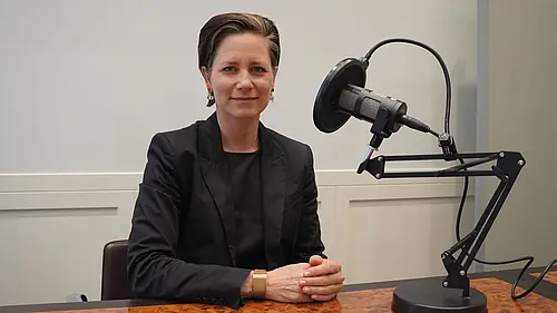 eine Frau vor einem Podcastmikro lächelt in die Kamera