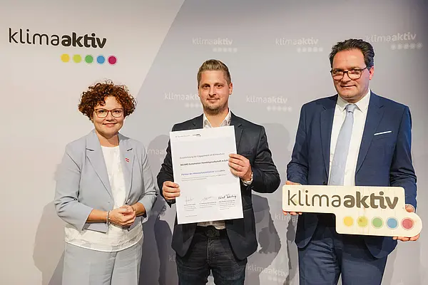 Menschen mit Urkunde und klimaaktiv Schild lächeln in die Kamera