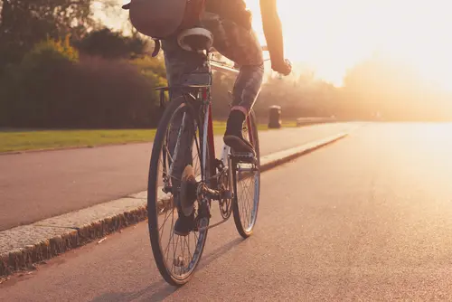 Radfahrer am Fahrrad auf einer Straße. Die Sonne scheint.