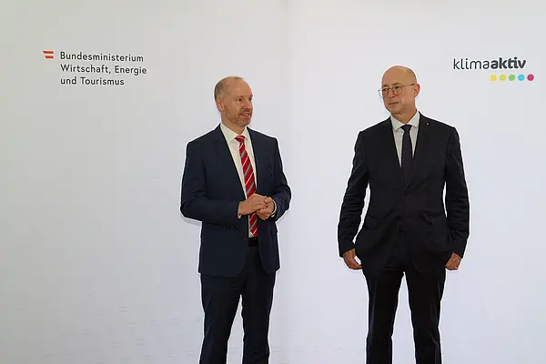 2 Männer in Anzug stehen vor einer Logowand klimaaktiv