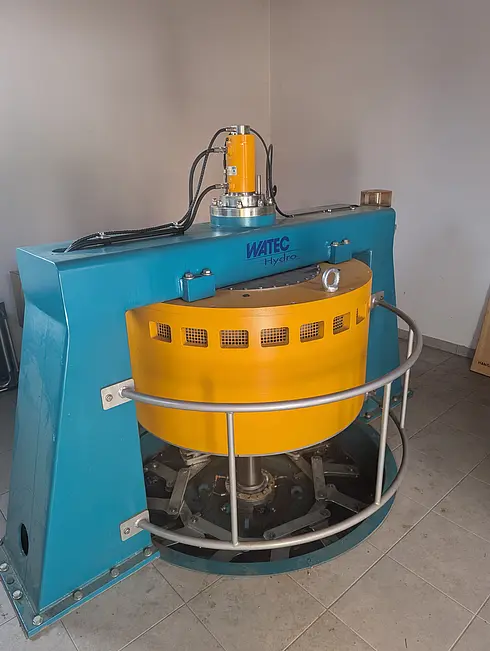 Eine blau-gelbe Wasserkraftturbine von Watec Hydro, installiert in einem Innenraum mit Fliesenboden.