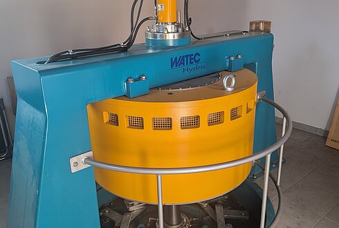 Eine blau-gelbe Wasserkraftturbine von Watec Hydro, installiert in einem Innenraum mit Fliesenboden.
