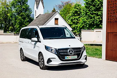 weißer Kleintransporter, rechts dekorative Säule eines Frieshofs, Kirche im Hintergrund