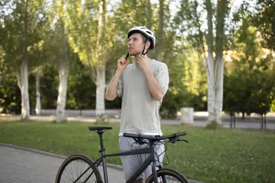 Mann setzt sich Fahrradhelm auf, sein Fahrrad angelehnt an seinen Körper. Im Hintergrund ein Park