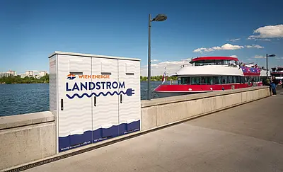 Links Kasten mit Aufschrift Wien Energie - Landstrom, rechts rotes Schiff, im Hintergrund Donau