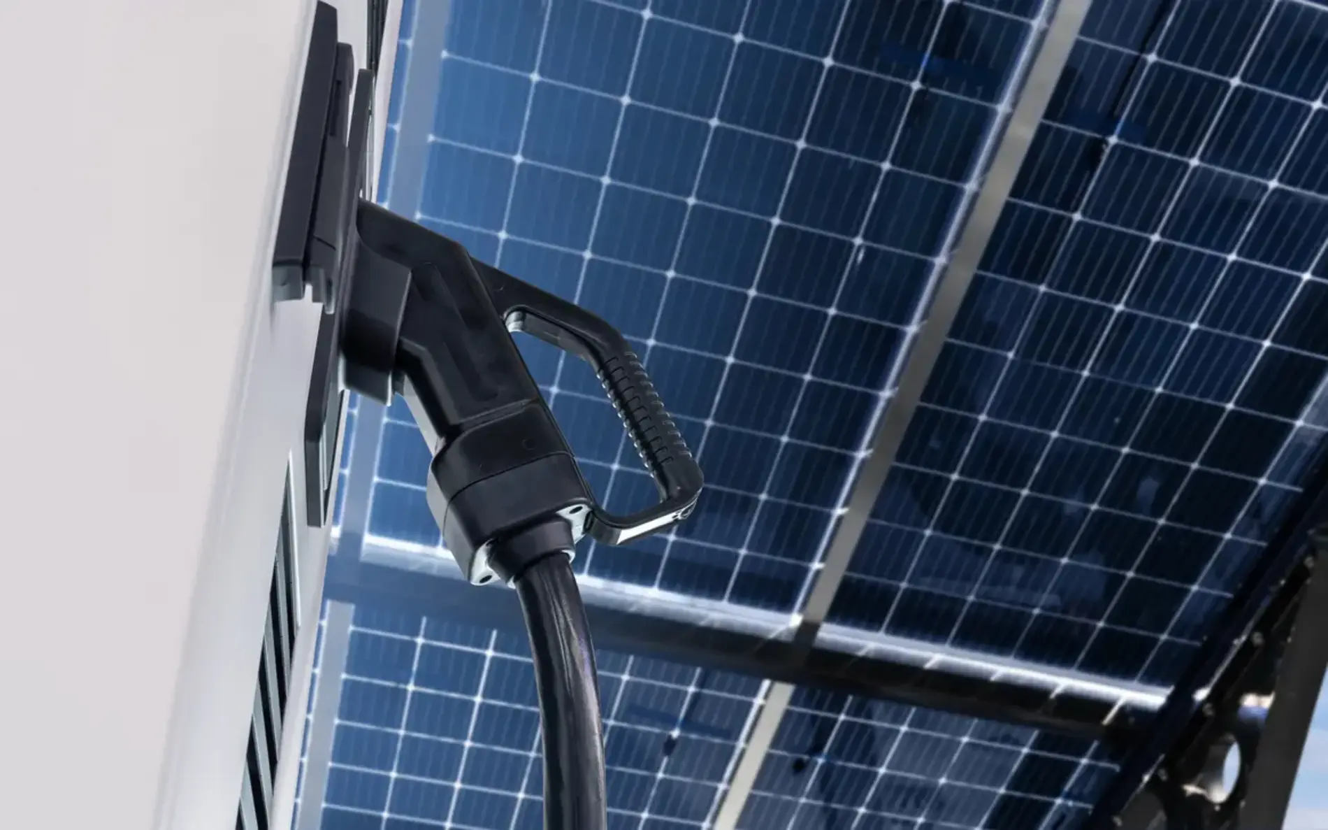 Elektroauto-Ladestation mit angeschlossenem Ladekabel unter einem großen Solarpanel bei blauem Himmel.