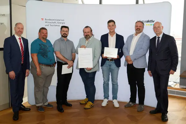 7 Personen mit Urkunde schauen in die Kamera