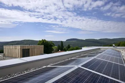 PV Anlage auf einem Dach dahinter ein Gebäude in Holzbauweise