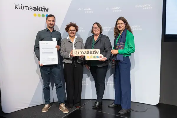4 Personen mit Urkunde und klimaaktiv Schild schauen in die Kamera