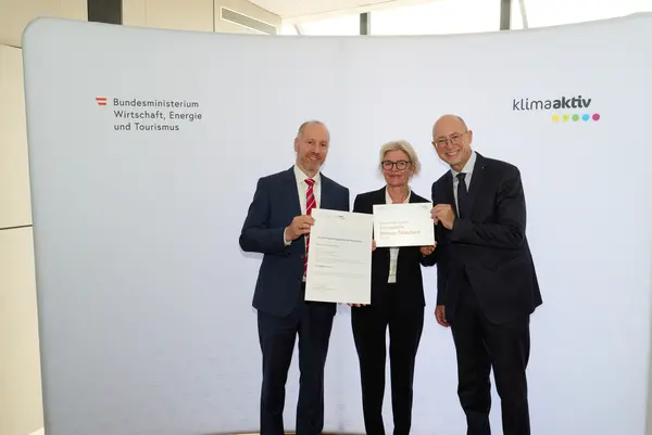 3 Personen mit Urkunde schauen in die Kamera