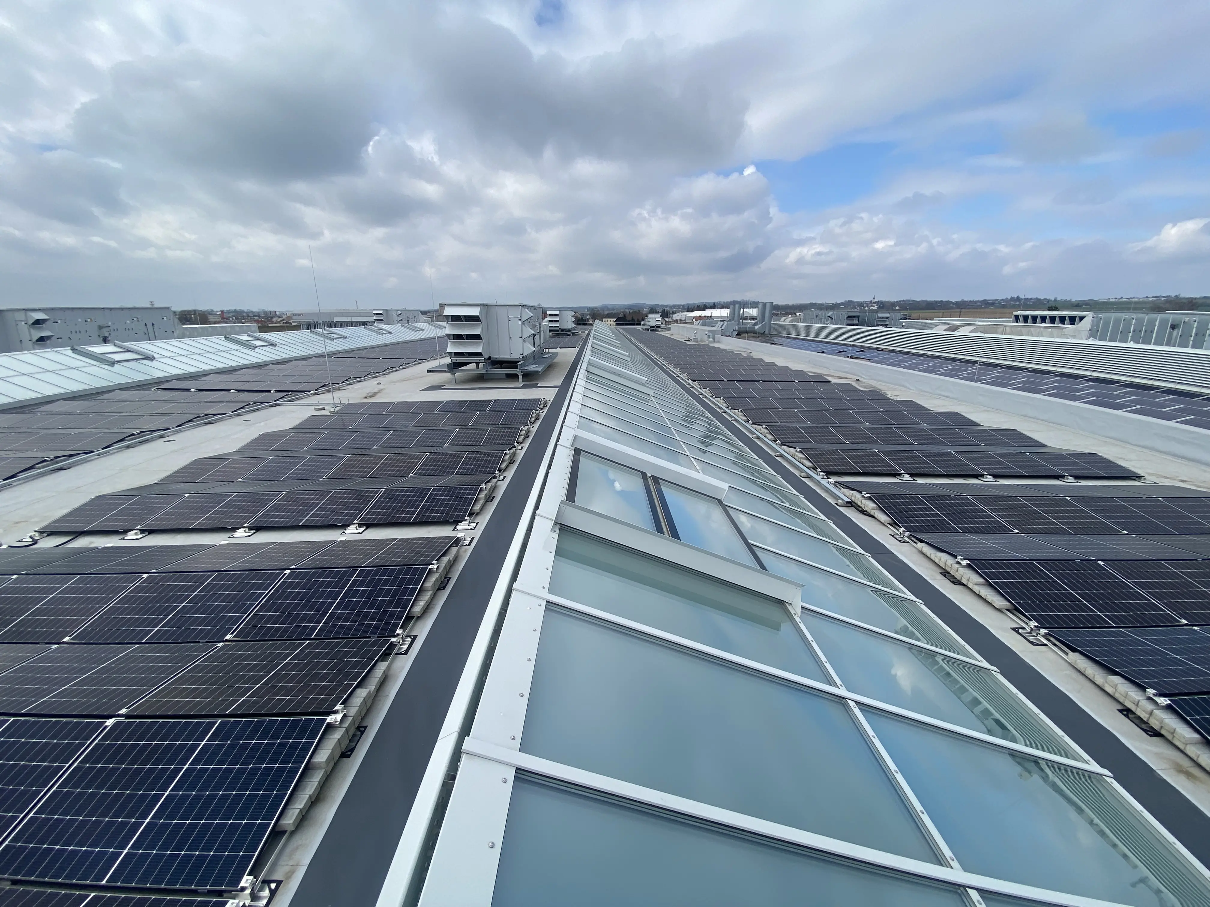 Solarmodule auf einem Dach neben langen Glas-Lichtbändern, die Tageslicht in die Produktionshalle bringen.