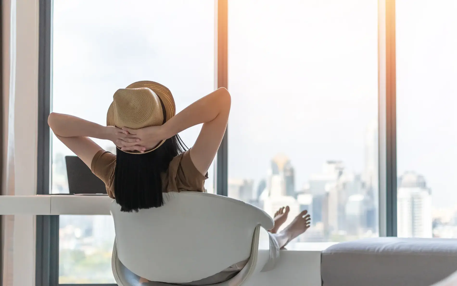 Eine Person sitzt entspannt auf einem Stuhl vor einem großen Fenster mit Blick auf eine Stadt.
