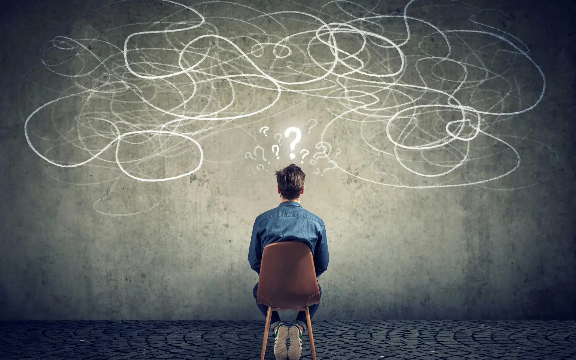 Mensch betrachtet eine Tafel, auf der mit Kreide Fragezeichen gemalt sind