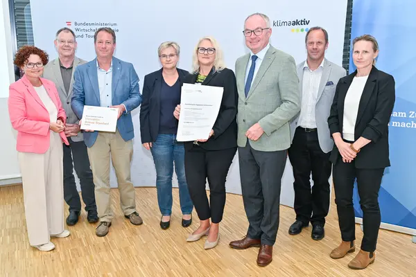 Personen mit Urkunde schauen in die Kamera