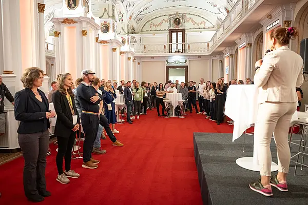 Moderation am Podium bittet 3 MEnschen auf die Bühne