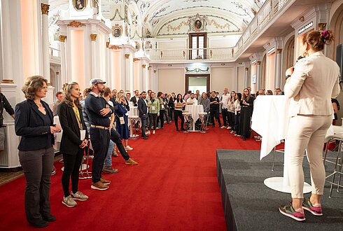Moderation am Podium bittet 3 MEnschen auf die Bühne