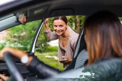 Eine Frau steigt zu einer anderen Frau ins Auto und lächelt dabei.