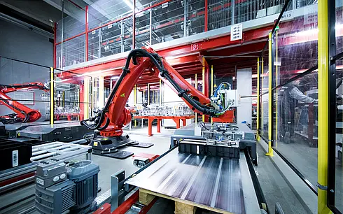 Roter Industrieroboter in einer modernen Produktionshalle, umgeben von Maschinen und Förderbändern.