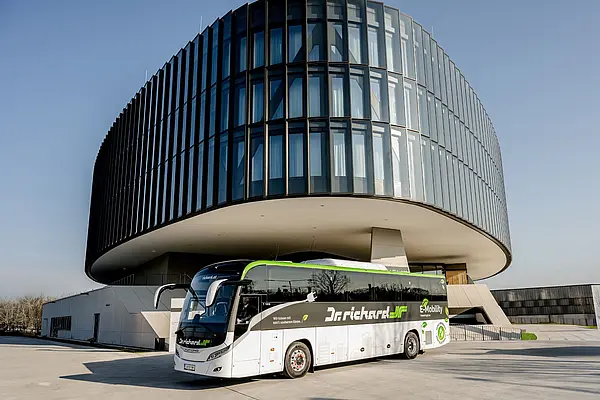 elektrischer Reisebus steht vor futuristischem, rundem Gebäude mit Glasfront