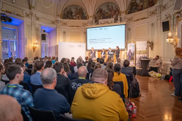 Prunkvoller Saal mit vielen Menschen, die sitzend lauschen