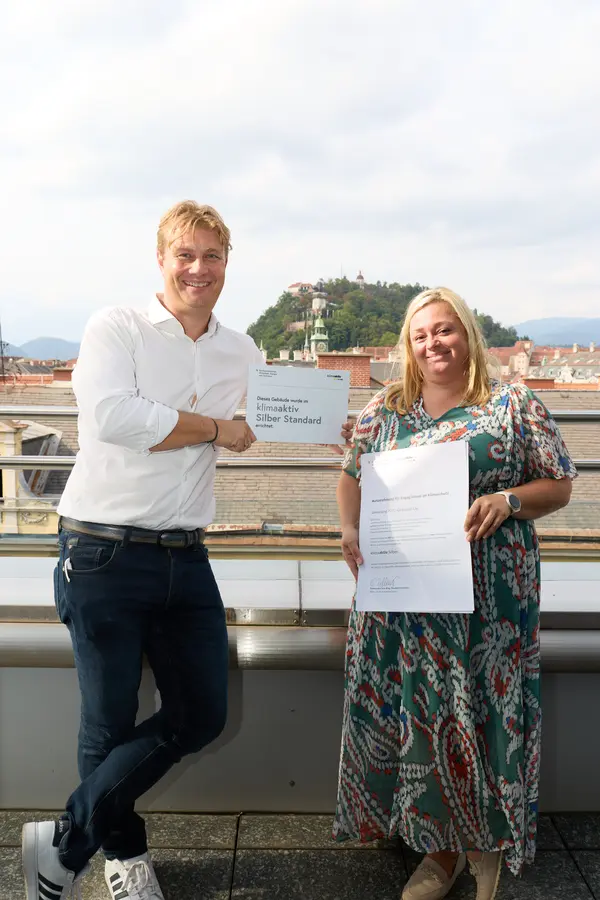 2 Personen mit Urkunde schauen in die Kamera