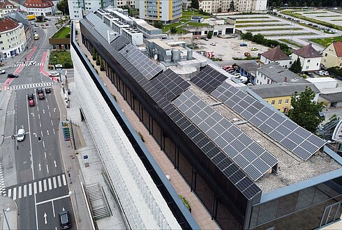 Luftaufnahme eines Gebäudedachs mit umfangreicher Solaranlage, umgeben von städtischer Bebauung.