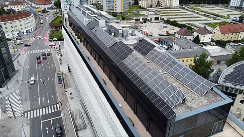 Luftaufnahme eines Gebäudedachs mit umfangreicher Solaranlage, umgeben von städtischer Bebauung.