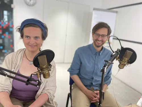 Petra Jens und Martin Blum mit Tisch-Mikrofonen vor dem Gesicht