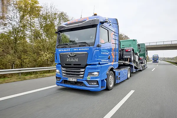 Blauer, elektrischer Sattelschlepper transportiert auf langem Anhänger zwei grüne Sattelschlepper auf der Autobahn