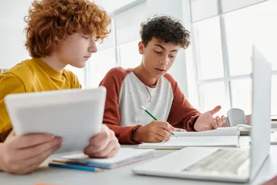Zwei Teenager sitzen am Tisch in einer Schule und schauen sich eine Aufgabe am Zettel an