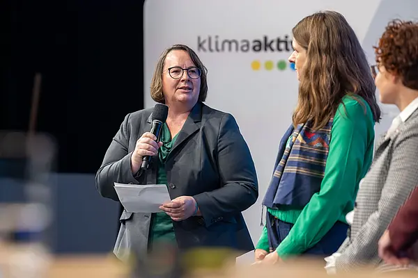 Frau spricht in ein Mikro auf einer Bühne