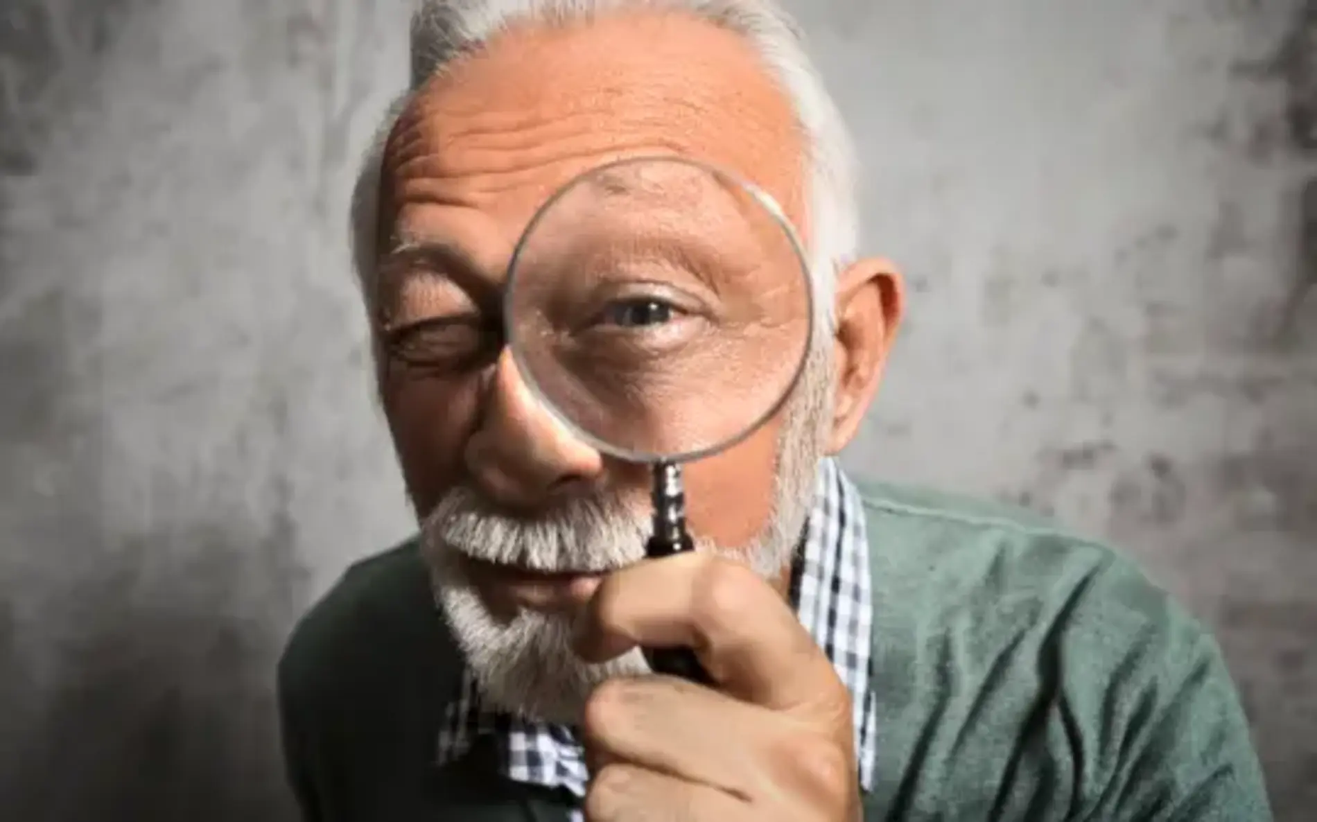 Ein Älterer Mann schaut durch eine größere Lupe in die Kamera