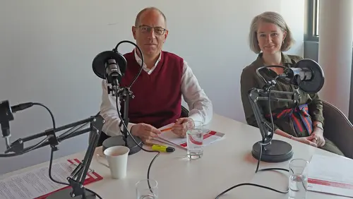 2 Menschen vor Mikrofonen lächeln in die Kamera