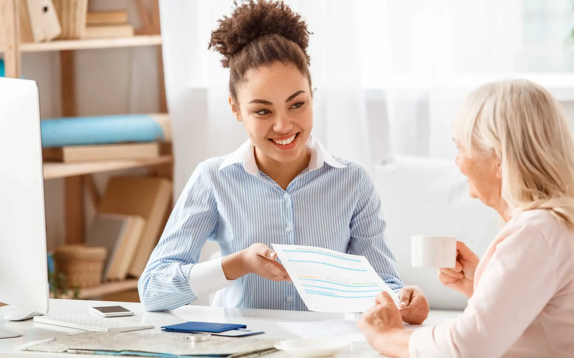 Eine Frau präsentiert an einem Tisch einen Zettel einer anderen frau, die mit einer Tasse am Tisch sitzt. 
