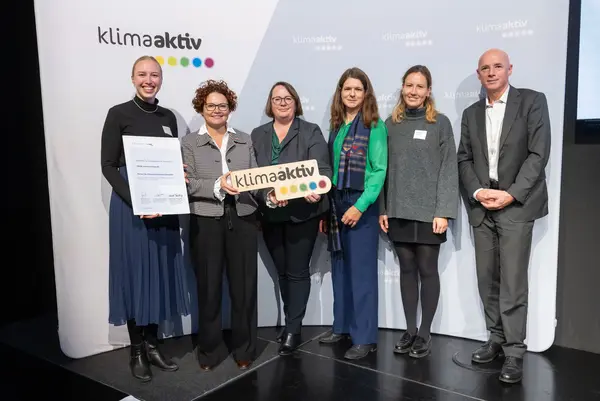 6 Personen mit Urkunde und klimaaktiv Schild schauen in die Kamera