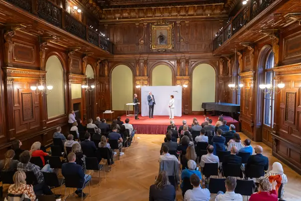 ein Festsaal mit Bühne, Publikum und Menschen auf der Bühne