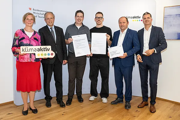 eine Gruppe von Menschen auf einer Bühne hält Urkunden in die Kamera