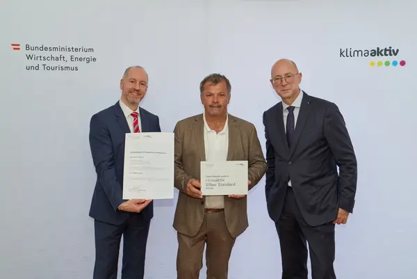 3 Personen mit Urkunde schauen in die Kamera