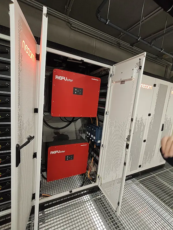 Geöffneter Batteriespeicher-Schrank mit zwei roten Wechselrichtern und Verkabelung, Teil eines industriellen Energiespeichersystems.