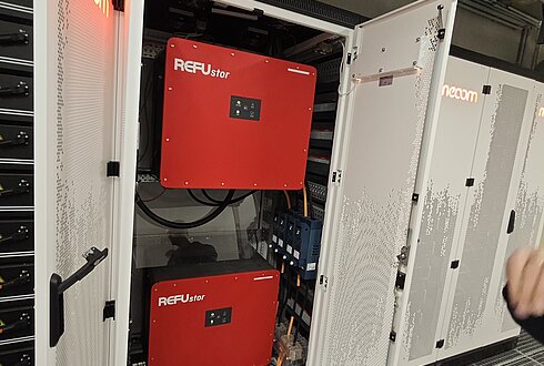 Geöffneter Batteriespeicher-Schrank mit zwei roten Wechselrichtern und Verkabelung, Teil eines industriellen Energiespeichersystems.